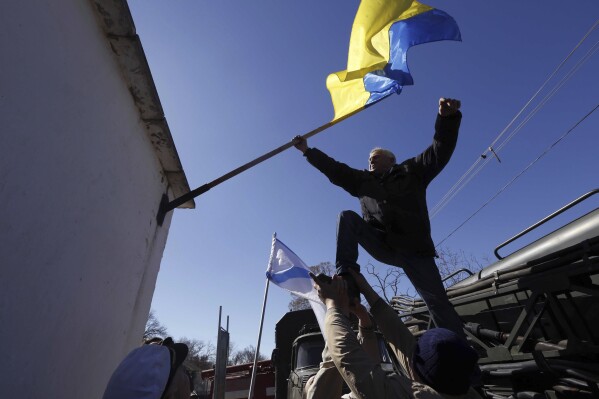 FILE - A man removes a Ukrainian flag after seizure of the base in Novofedorivka, Crimea, Saturday, March 22, 2014. The Crimean Peninsula's balmy beaches have been vacation spots for Russian czars and has hosted history-shaking meetings of world leaders. And it has been the site of ethnic persecutions, forced deportations and political repression. Now, as Russia’s war in Ukraine enters its 18th month, the Black Sea peninsula is again both a playground and a battleground. (AP Photo, File)