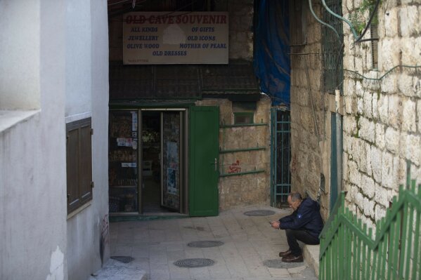 A Palestinian vendor sits in front of his shop near the Church of the Nativity, traditionally believed to be the birthplace of Jesus Christ, in the West Bank City of Bethlehem, Monday, Nov. 23, 2020. Normally packed with tourists from around the world at this time of year, Bethlehem resembles a ghost town – with hotels, restaurants and souvenir shops shuttered by the pandemic. (AP Photo/Majdi Mohammed)
