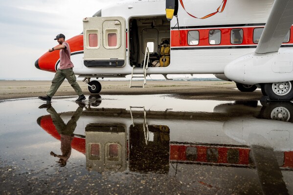 U.S. Forest Service smokejumper Mike Dunn steps through a puddle while exiting a plane in Fort St. John, British Columbia, Wednesday, July 5, 2023. His crew is assisting Canadian firefighters battling fires throughout the region. (AP Photo/Noah Berger)