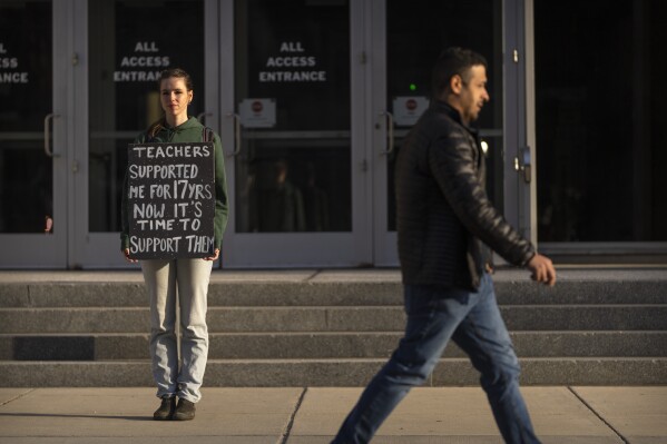 Chloe Kienzle of Arlington, Va., holds a sign as she stands outside the headquarters of the U.S. Department of Eduction, which were ordered closed for the day for what officials described as security reasons amid large-scale layoffs, Wednesday, March 12, 2025, in Washington. (AP Photo/Mark Schiefelbein)