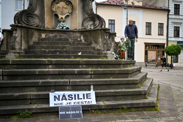 A man walks with a child next to a banner that reads "Violence is Not the Way" and " No Violence" in Banska Bystrica, central Slovakia, Friday, May 17, 2024. When a gunman shot Slovak Prime Minister Robert Fico this week, shock rippled across the Central European country — even though the pro-Russia leader himself warned that the country was so divided that an assassination attempt was possible. (AP Photo/Denes Erdos)