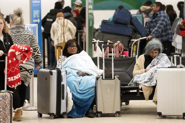 Ana Rosario of Houston, sitting left, tries to keep warm as she waits on her flight in Terminal A at Houston George Bush Intercontinental Airport Tuesday, Jan. 16, 2024, in Houston. (Melissa Phillip/Houston Chronicle via AP)