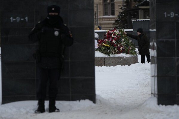 A policeman guards as a young man lay flowers paying the last respect to Alexei Navalny at the monument, a large boulder from the Solovetsky islands, where the first camp of the Gulag political prison system was established, near the historical the Federal Security Service (FSB, Soviet KGB successor) building, in Moscow, Russia, on Saturday morning, Feb. 17, 2024. Russian authorities say that Alexei Navalny, the fiercest foe of Russian President Vladimir Putin who crusaded against official corruption and staged massive anti-Kremlin protests, died in prison. He was 47. (AP Photo/Alexander Zemlianichenko)