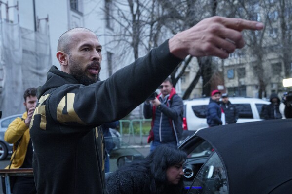 Andrew Tate gestures upon exiting a police detention facility in Bucharest, Romania, Tuesday, March 12, 2024. A court in Romania's capital has granted a request by British authorities to extradite the divisive online influencer Andrew Tate but only after legal proceedings against him in Romania have been concluded. (AP Photo/Andreea Alexandru)