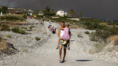 A man carries a child as they leave an area where a forest fire burns, on the island of Rhodes, Greece, Saturday, July 22, 2023. A large wildfire burning on the Greek island of Rhodes for a fifth day has forced authorities to order an evacuation of four locations, including two seaside resorts. (Lefteris Diamanidis/InTime News via AP)