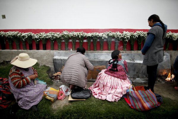 In this picture taken Jan. 7, 2020, women sit at the edge of a cemetery in La Paz, Bolivia, paying homage to unidentified deceased loved ones, who they call the forgotten souls. The women light candles, throw coca leaves and cigarettes bunched together in the traditional indigenous blessing. (AP Photo/Natacha Pisarenko)