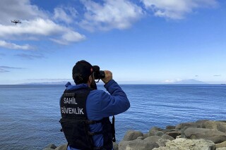 A member of Turkish Coastal Security uses binoculars on the Turkey's shore of Aegean sea in Eceabat, Turkey, Friday, March 15, 2024. A rubber dinghy carrying migrants sank off Turkey's northern Aegean coast on Friday, killing at least 22 people, officials said. (Dia Images via AP)