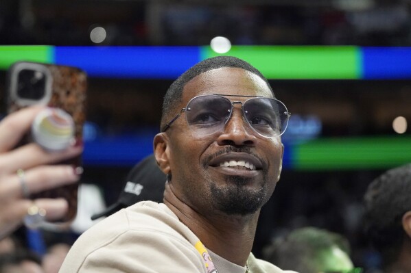 FILE - Jamie Foxx smiles during an NBA basketball game between the Washington Wizards and Dallas Mavericks in Dallas, Saturday, Nov. 27, 2021. Academy Award winning actor, Grammy winning singer and comedian says he “went to hell and back” but is recovering from an undisclosed medical condition. Foxx made his first public comments in an Instagram message posted on Friday, July 21, 2023 after being hospitalized in April. (AP Photo/LM Otero, File)