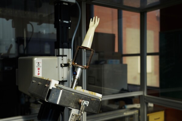 A latex dipping machine spins around after dipping a model glove mold into guayule latex, Tuesday, Feb. 6, 2024, in Wooster, Ohio. With climate change bearing down on agriculture around the world, the need for crops like guayule that can withstand extreme weather such as persistent drought is important. (AP Photo/Joshua A. Bickel)