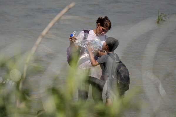 Migrants stop for a water break as they walk in the Rio Grande behind concertina wire as they try to enter the U.S. from Mexico in Eagle Pass, Texas, Tuesday, July 11, 2023. (AP Photo/Eric Gay)