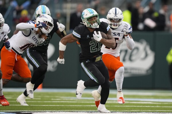 Tulane running back Makhi Hughes (21) carries past UTSA linebackers Martavius French (10) and Avery Morris on a 58-yard run in the first half of an NCAA college football game in New Orleans, Friday, Nov. 24, 2023. (AP Photo/Gerald Herbert)