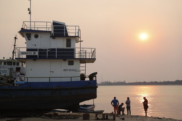 Workers rest at sunset on the shore of the Paraguay River in Asuncion, Paraguay, Wednesday, Oct. 7, 2020. The Paraguay River reached its lowest level in 50 years on Friday, Oct. 9, 2020, following months of extreme drought, which has exposed the nation’s economic dependence on the river and limited access to drinking water. (AP Photo/Jorge Saenz)