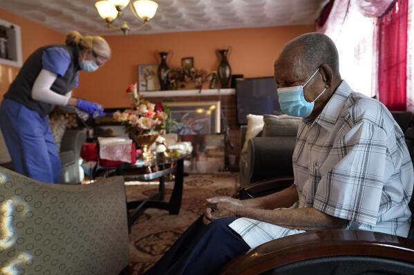 FILE - In this Feb. 11, 2021, file photo Edouard Joseph, 91, right, clasps his hands as geriatrician Megan Young, left, prepares to give him a COVID-19 vaccination at his home in the Mattapan neighborhood of Boston. A majority of Americans agree that government should help people fulfill a widely held aspiration to age in their own homes, not institutional settings, according to a new survey from The Associated Press-NORC Center for Public Affairs Research. (AP Photo/Steven Senne, File)
