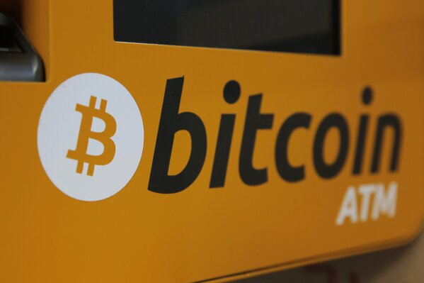 FILE - In this Dec. 21, 2017 file photo, a Bitcoin logo is shown is displayed on an ATM in Hong Kong, Thursday, Dec. 21, 2017. Tesla says it has invested more than $1 billion in Bitcoin and will accept the digital currency as payment for its electric vehicles. In a regulatory filing Monday, Feb. 8, 2021, Elon Musk’s electric vehicle company said its board approved of the $1.5 billion investment and potentially more in the future.  (AP Photo/Kin Cheung, File)