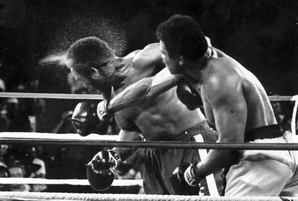 Perspiration flies from the head of George Foreman as he takes a right from challenger Muhammad Ali in the seventh round in the match dubbed Rumble in the Jungle in Kinshasa, Zaire, Oct. 30, 1974. (AP Photo/Ed Kolenovsky, File)