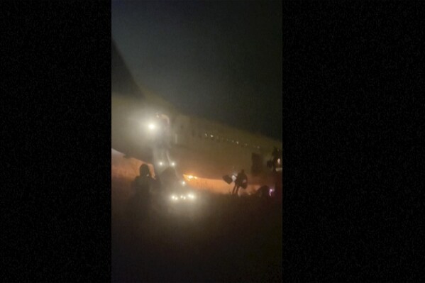 In this grab taken from video people jump down emergency slides, running from a plane, in Dakar, Senegal, Wednesday, May 8, 2024. A Boeing 737 plane carrying 85 people caught fire and skidded off a runway at the airport in Dakar, Senegal’s capital, injuring 10 people. (Cheick Siriman Sissoko via AP)