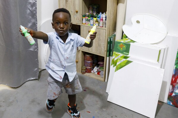 Ace Liam Nana Sam Ankrah, who turns 2 years old in July, displays his paint tubes at his mother's art gallery in Accra, Ghana, Monday, May 27, 2024. Ankrah holds the record as the world's youngest male artist.  His mother, Chantelle Cocoa-Egan, says it all started by chance when her son, who was six months old at the time, discovered her paints.  (AP Photo/Misper Apawu)