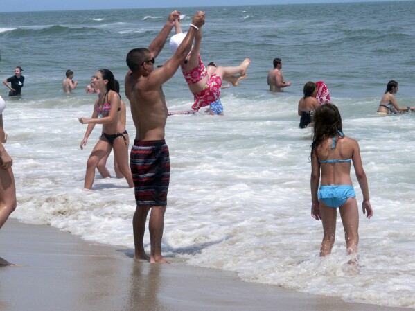 Beachgoers play in the surf in Ship Bottom, N.J. on June 30, 2014. On Aug. 4, 2023, a German wind power company and a New York utility applied for permission to build a wind farm 37 miles off the coast of Long Beach Island, far enough out to sea that it could not be seen from the beach. (AP Photo/Wayne Parry)