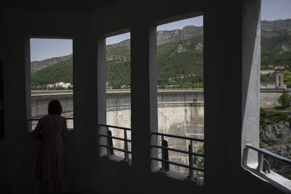 A Swiss tourist looks out at the hydroelectric dam of Lac de Castillon in southern France, Tuesday, June 20, 2023. Human-caused climate change is lengthening droughts in southern France, meaning the reservoirs are increasingly drained to lower levels to maintain the power generation and water supply needed for nearby towns and cities.(AP Photo/Daniel Cole)