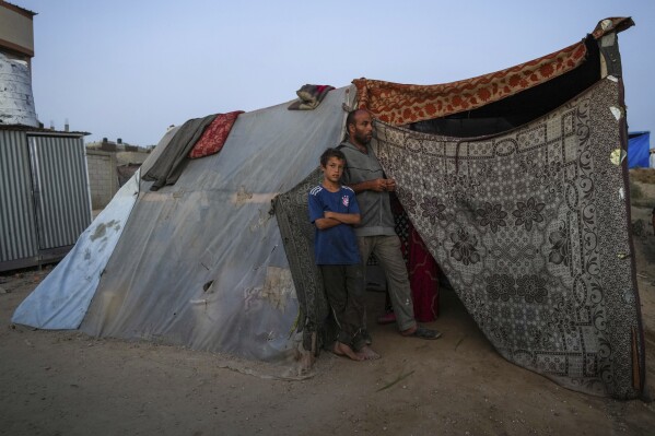 Abdelsattar al-Batsh stands with his son ahead of the Eid al-Adha holiday in Deir al Balah, Gaza Strip, Tuesday, June 11, 2024. They were displaced from their home by the war between Israel and Hamas. (AP Photo/Abdel Kareem Hana)