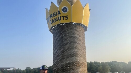 This photo provided by the Georgia Peanut Commission shows Cole Sercer of Sercer Machine & Fabrication, standing beside the Big Peanut that he and his employees designed and built near Interstate 75 in Ashburn, Ga., Thursday, July 20, 2023. The monument replaces a similar peanut that blew down during Hurricane Michael in October 2018. (Joy Crosby/Georgia Peanut Commission via AP)