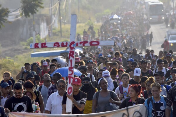 Migrants walking on the highway carry a cross that reads in Spanish 
