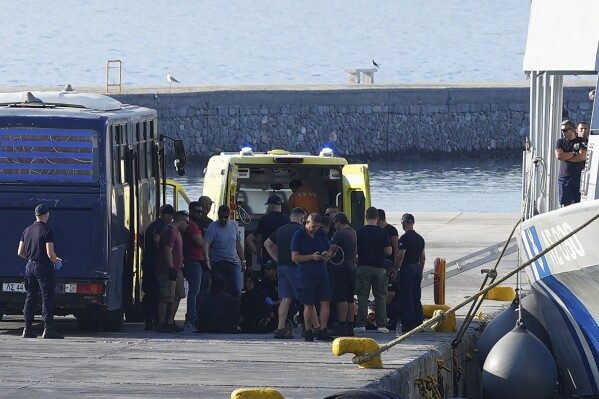 Migrantes rodean una ambulancia tras un rescate realizado por la guardia costera en el puerto de Mytilene en la isla egea de Lesbos, Grecia, 28 de agosto de 2023. (AP Foto/Panagiotis Balaskas)