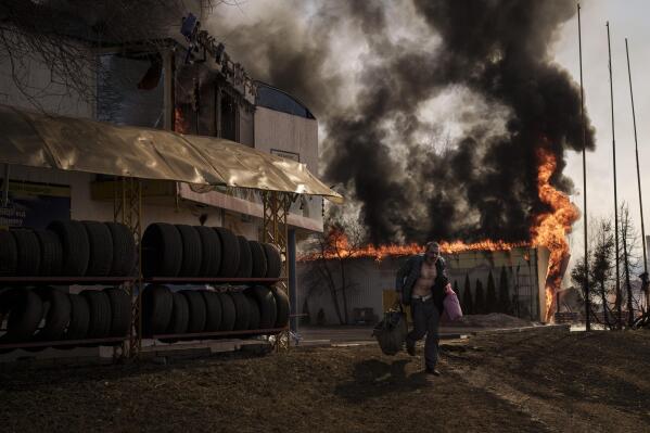 A man runs after recovering items from a burning shop following a Russian attack in Kharkiv, Ukraine, Friday, March 25, 2022. (AP Photo/Felipe Dana)