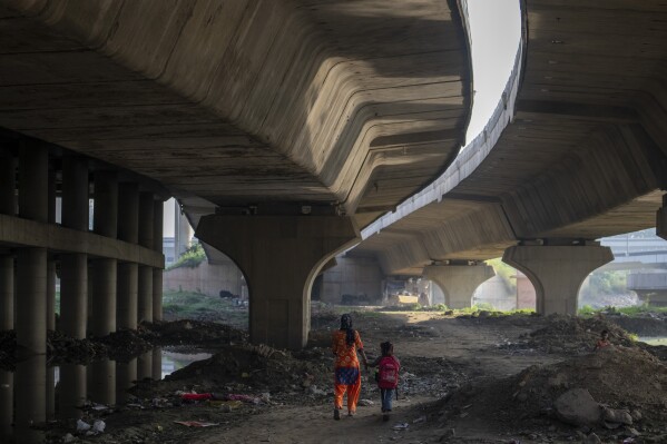 Meera Devi, left, accompanies her daughter Arima, 7, to her school as they walk on the flood plain of Yamuna River, in New Delhi, India, Friday, Sept. 29, 2023. Their family was among those displaced by the recent floods in the Indian capital's Yamuna River. Storms, floods, fires and other extreme weather events led to more than 43 million displacements involving children between 2016 and 2021, according to a United Nations report. (AP Photo/Altaf Qadri)