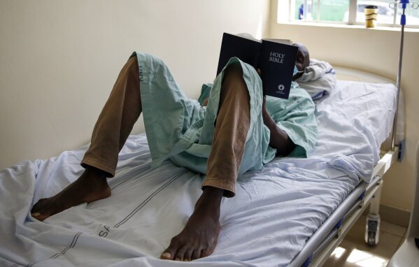 FILE - In this Friday, May 1, 2020 file photo, a patient lies on his bed reading the Bible in a ward for those who have tested positive for the new coronavirus, at the infectious disease unit of Kenyatta National Hospital, located at Mbagathi Hospital, in Nairobi, Kenya. The COVID-19 pandemic is testing the patience of some religious leaders across Africa who worry they will lose followers, and funding, as restrictions on gatherings continue. (AP Photo/Brian Inganga, File)