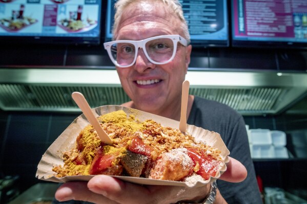 Lars Obendorfer, owner of "Best Worscht in Town" sausage holds up vegan curry wursts in one of his branches in Frankfurt, Germany, Tuesday, Sept. 5, 2024. “There was downright hostility between the meat eaters and the vegans,” he says. “And I just couldn’t understand it, and I said, ‘knock off the arguing.’” (AP Photo/Michael Probst)