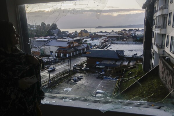 A woman looks through her home's broken window at more damage the day after tornado hit Puerto Varas, Chile, Monday, May 26, 2025. (AP Photo/Patricio Aguayo)