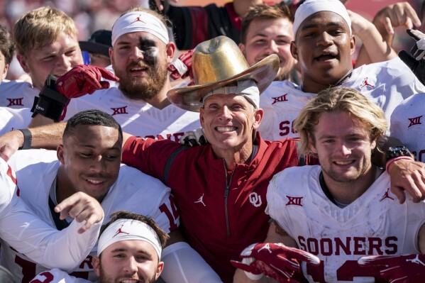 Oklahoma head coach Brent Venables wears the Golden Hat as he takes a group photo with his team after their 34-30 victory over Texas in an NCAA college football game at the Cotton Bowl, Saturday, Oct. 7, 2023, in Dallas. (AP Photo/Jeffrey McWhorter)