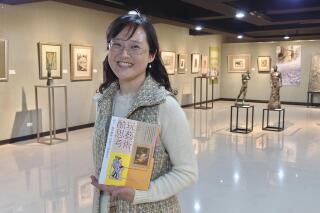 In this photo taken on March 23, 2021, Taiwanese author Iris Chiang holds her book "Play with Art" at the saloon featuring Taiwanese artist YUYU Yang's work in Taipei, Taiwan. Four years on after being sold to a Chinese publisher and no going to press, Chiang's book that teaches children how to appreciate art has fallen victim to the heightened tensions between China and Taiwan that are spilling over into the cultural sphere. (AP Photo/Chiang Ying-ying)