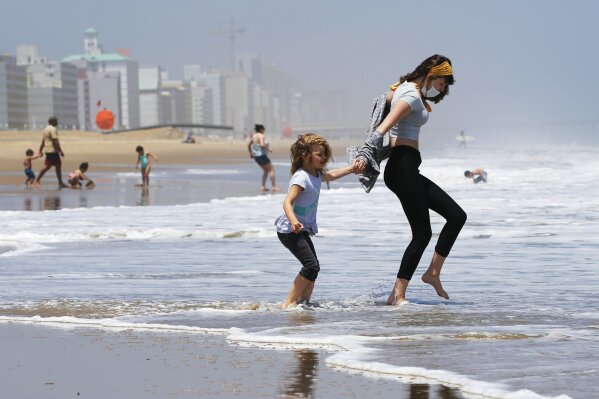 FILE - In this May 22, 2020, file photo, Victoria Faughnan, right, and Evelyn Faughnan, play in the surf in Virginia Beach, Va., the day the state reopened the beachfront during the coronavirus pandemic. The pandemic not only upended the tourism industry, but how states, cities and attractions market themselves as summer travel destinations. (AP Photo/Steve Helber, File)