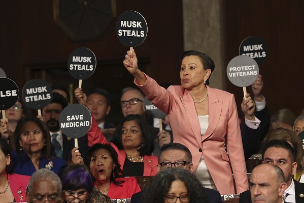 Rep. Nydia Velazquez, D-N.Y., holds a protest sign with fellow Democrats as President Donald Trump addresses a joint session of Congress at the Capitol in Washington, Tuesday, March 4, 2025. (Win McNamee/Pool Photo via AP)