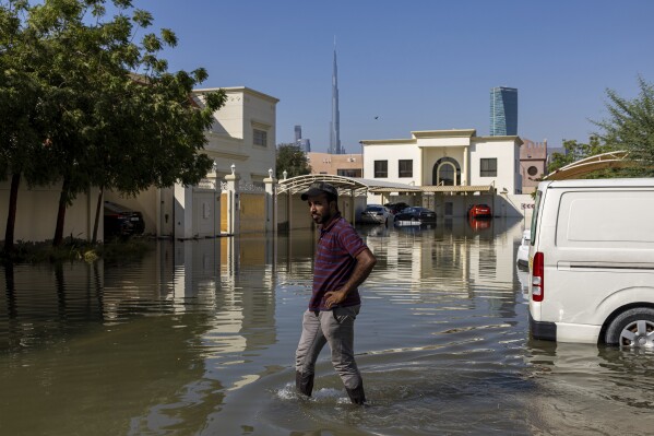 FILE - A man walks through standing floodwater caused by heavy rain with the Burj Khalifa, the world's tallest building, seen in Dubai, United Arab Emirates, April 18, 2024. A new report says climate change played a role in the floods. (AP Photo/Christopher Pike, File)