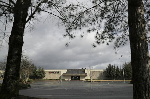 The parking lot in front of a closed Macy's store is empty, Monday, March 30, 2020, at a mall in Olympia, Wash. Macy's says it will stop paying tens of thousands of employees who were left out of work when the chain closed its stores earlier in the month in response to collapsing sales during the new coronavirus pandemic. (AP Photo/Ted S. Warren)