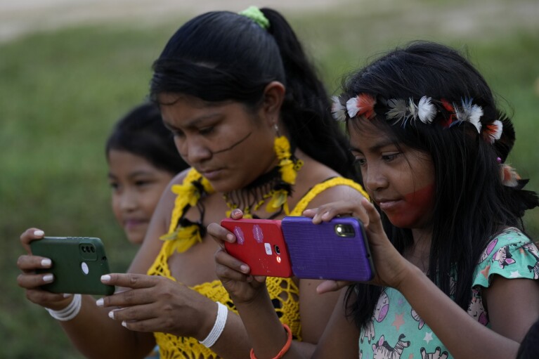 An Indigenous Tembe mother and her daughters take photos in the Tenetehar Wa Tembe village, located in the Alto Rio Guama Indigenous territory of the Paragominas municipality in the Para state of Brazil, Tuesday, May 30, 2023. (AP Photo/Eraldo Peres)