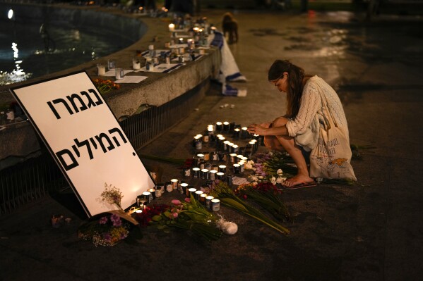 A woman lights candles in honor of victims of the Hamas attacks during a vigil at Dizengoff square in central Tel Aviv, Israel, Friday, Oct. 13, 2023. The sign reads: "Out of Words." (AP Photo/Francisco Seco)