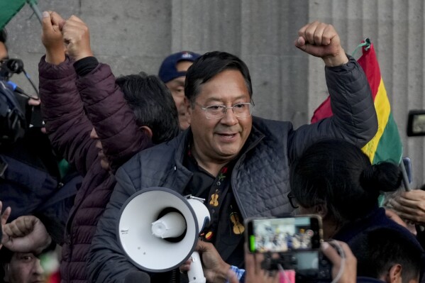 Bolivian President Luis Arce raises a clenched fist surrounded by supporters and media, outside the government palace in La Paz, Bolivia, Wednesday, June 26, 2024. Armored vehicles rammed the doors of Bolivia's government palace Wednesday in an apparent coup attempt against Arce, but he vowed to stand firm and named a new army commander who ordered troops to stand down. (AP Photo/Juan Karita)