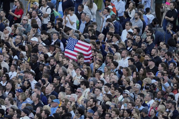 People hold up a US flag as the newly elected Pope Leo XIV appears at the balcony of St. Peter's Basilica at the Vatican, Thursday, May 8, 2025. (AP Photo/Markus Schreiber)