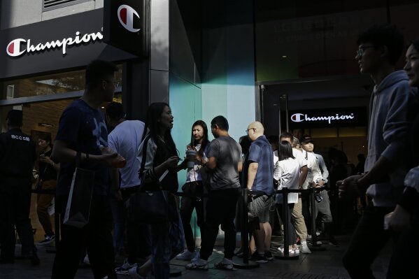 
              People walk by shoppers queue in line to enter a sportswear from American brand Champion, at the capital city's popular shopping mall in Beijing, Monday, Sept. 24, 2018. China raised tariffs Monday on thousands of U.S. goods in an escalation of its fight with President Donald Trump over technology policy and accused Washington of bullying Beijing and damaging the global economy. (AP Photo/Andy Wong)
            
