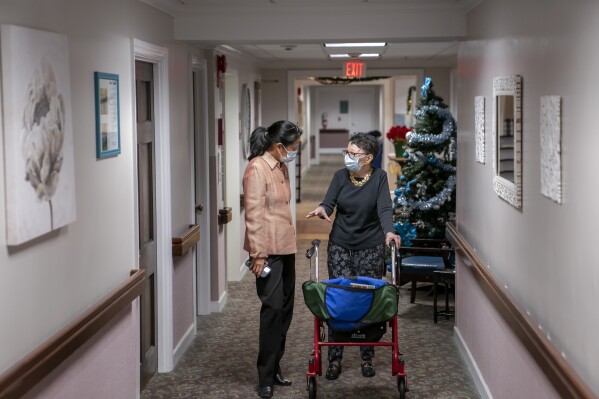 FILE - Tina Sandri, CEO of Forest Hills of DC senior living facility, left, helps resident Courty Andrews back to her room, Dec. 8, 2022, in Washington. The federal government will, for the first time, dictate staffing levels at nursing homes, the Biden administration said Friday, Sept. 1, 2023, responding to systemic problems bared by mass COVID deaths. (AP Photo/Nathan Howard, File)