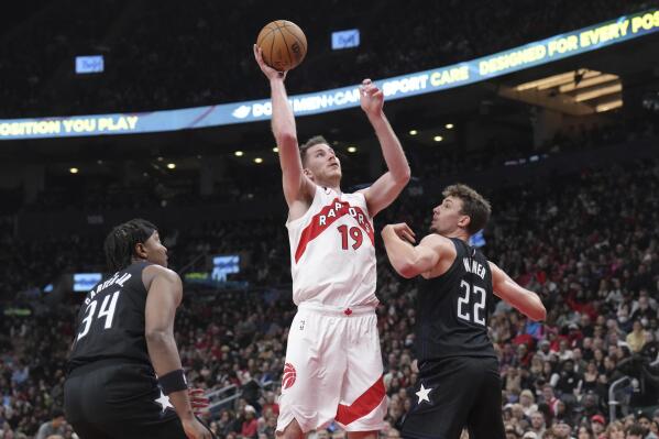 Toronto Raptors' Jacob Poeltl (19) scores on Orlando Magic's Wendell Carter Jr. (34) and Franz Wagner (22) during the first half of an NBA basketball game in Toronto on Tuesday, Feb. 14, 2023. (Chris Young/The Canadian Press via AP)