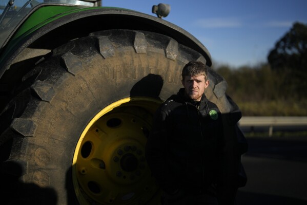 FILE - A farmer stands next to his tractor during a highway blockade in Villabet, south of Paris, on Friday, January 26, 2024.  (AP Photo/Thibault Camus, File)