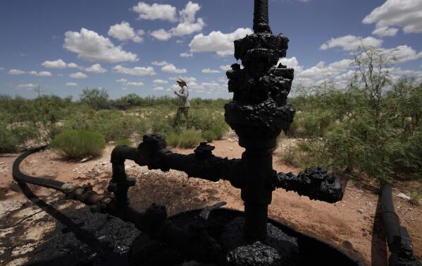 Ashley Williams Watt walks near a wellhead and flowline at her ranch, Friday, July 9, 2021, near Crane, Texas. The wells on Watt's property seem to be unplugging themselves. Some are leaking dangerous chemicals into the ground, which are seeping into her cattle's drinking water. And she doesn't know how long it's been going on. (AP Photo/Eric Gay)