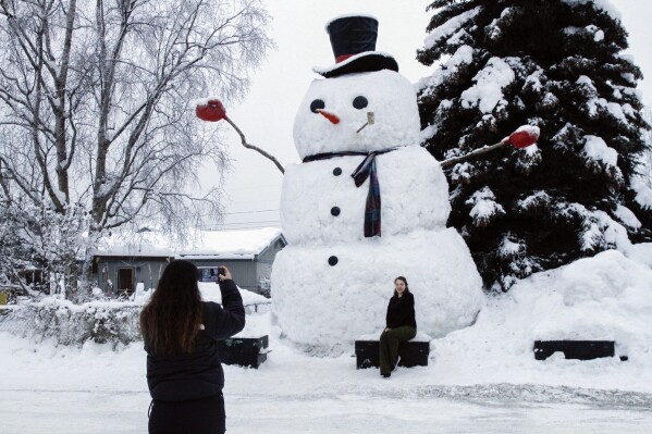 FILE - Isil Mico takes a photo of her sister-in-law Oznur Mico in front of Snowzilla, a snowman measuring more than 20 feet tall, in Anchorage, Alaska on Jan. 10, 2024. A recent storm dropped nearly 16 inches of snow on Anchorage, bringing the seasonal total to over 103 inches. It’s the earliest Alaska’s largest city has reached the 100-inch mark. (AP Photo/Mark Thiessen, File)