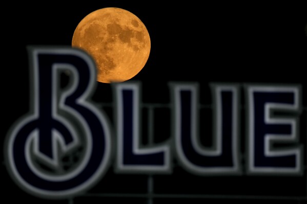 The blue supermoon rises beyond a sign in the outfield during a baseball game between the Kansas City Royals and the Pittsburgh Pirates on Wednesday, Aug. 30, 2023, in Kansas City, Mo. (AP Photo/Charlie Riedel)