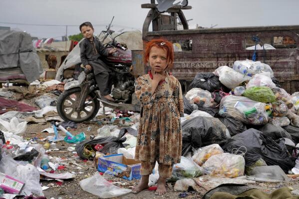 Two Afghan children stand amid piles of garbage next to their home, in Kabul, Afghanistan, April 18, 2022. (AP Photo/Ebrahim Noroozi)